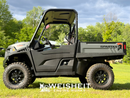 A black  Spartan side-by-side utility vehicle with off-road tires, parked outdoors on a grassy lawn with trees and a blue sky in the background. A vertical watermark is on the left side.